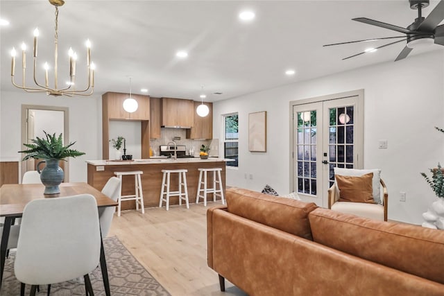 living room featuring ceiling fan with notable chandelier, sink, light hardwood / wood-style flooring, and french doors