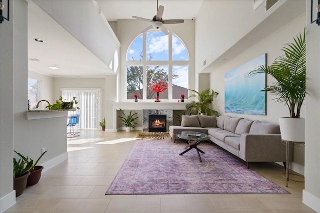 living room featuring a high end fireplace, a high ceiling, light tile patterned floors, and ceiling fan