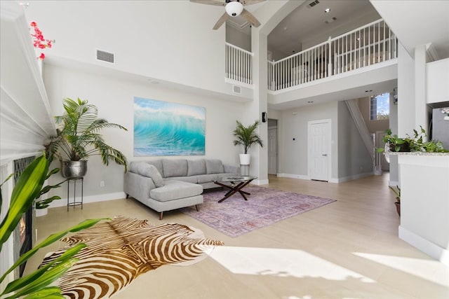 living room with ceiling fan, a towering ceiling, and light hardwood / wood-style floors