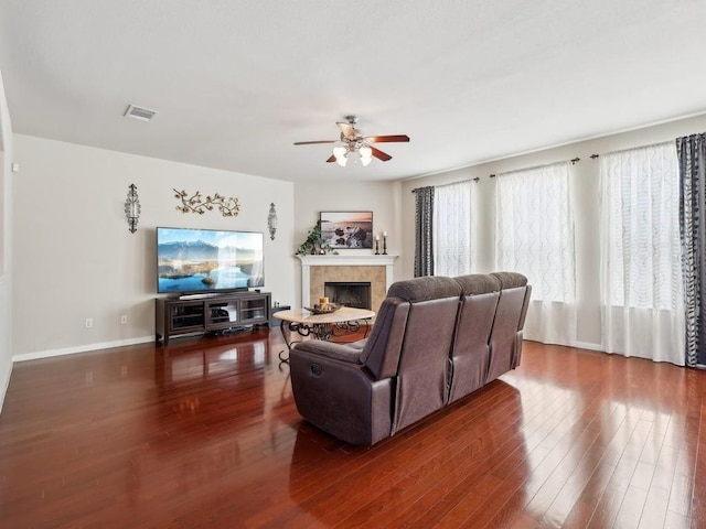 living room with a tile fireplace, dark wood-type flooring, and ceiling fan