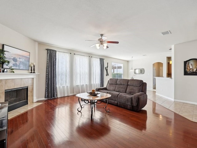 living room featuring ceiling fan, a tile fireplace, and light wood-type flooring