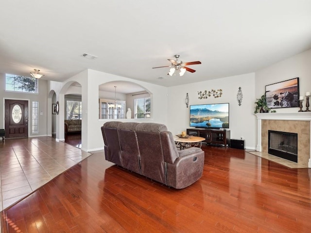 living room featuring dark hardwood / wood-style flooring, a tiled fireplace, and ceiling fan with notable chandelier