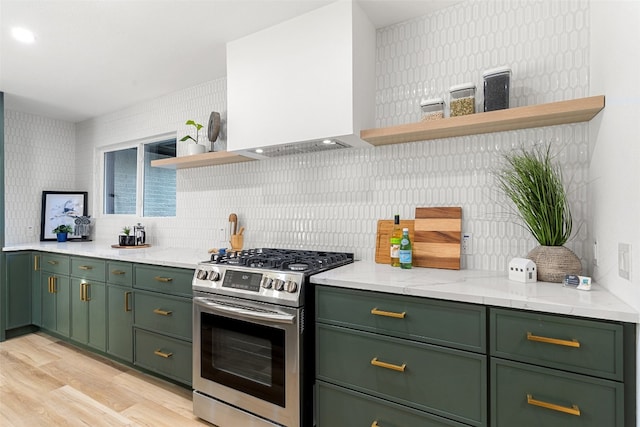 kitchen featuring stainless steel range with gas cooktop, green cabinetry, wall chimney exhaust hood, light stone countertops, and light wood-type flooring