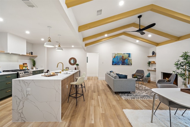 kitchen with ceiling fan, lofted ceiling with beams, light hardwood / wood-style floors, decorative light fixtures, and a center island with sink