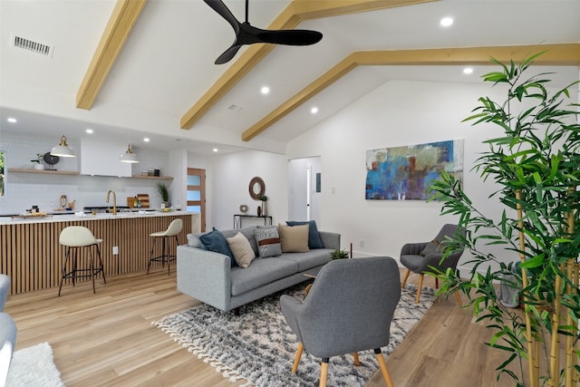 living room with ceiling fan, sink, beam ceiling, high vaulted ceiling, and light hardwood / wood-style flooring