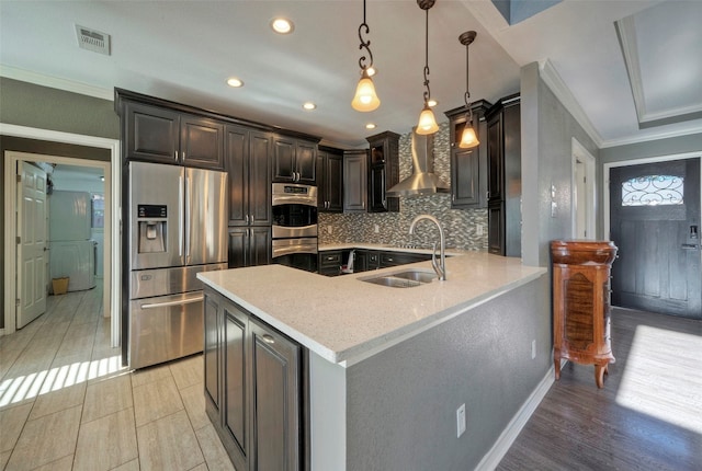 kitchen with wall chimney range hood, light wood-type flooring, appliances with stainless steel finishes, decorative light fixtures, and kitchen peninsula