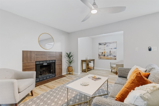 living room featuring a tile fireplace, light wood-type flooring, and ceiling fan