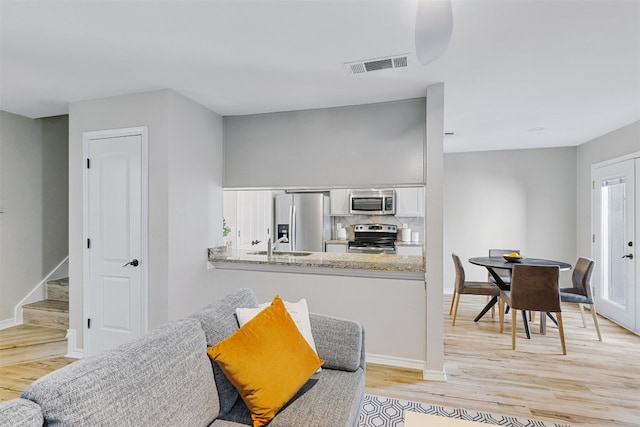 kitchen featuring kitchen peninsula, tasteful backsplash, stainless steel appliances, light hardwood / wood-style flooring, and white cabinetry