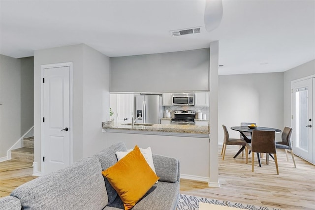 6700 Cooper Ln Unit 9, Austin, TX 78745 - kitchen with stainless steel appliances, white cabinetry, light wood finished floors, decorative backsplash, and a peninsula