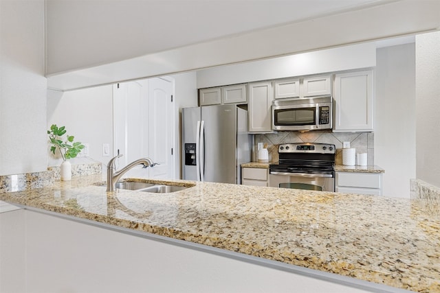 kitchen featuring backsplash, sink, light stone countertops, kitchen peninsula, and stainless steel appliances