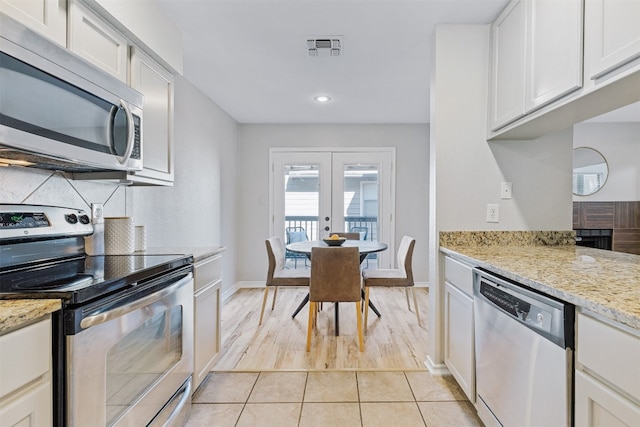 kitchen featuring light stone countertops, appliances with stainless steel finishes, french doors, light tile patterned floors, and white cabinetry