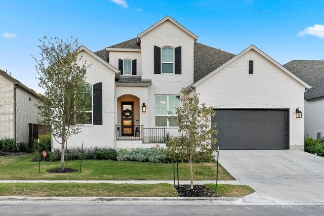 french country style house with covered porch, a garage, and a front lawn