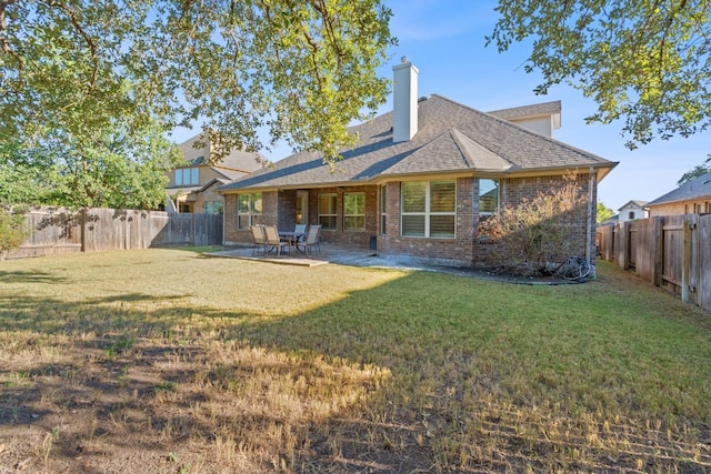 back of property featuring brick siding, a lawn, a fenced backyard, and roof with shingles