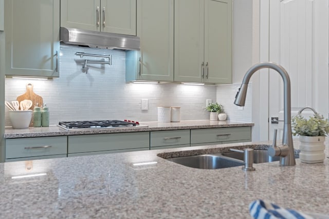 kitchen featuring light stone countertops, stainless steel gas cooktop, a sink, decorative backsplash, and under cabinet range hood