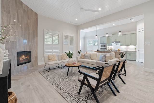 living room with a tiled fireplace, wooden ceiling, ceiling fan, and light wood-type flooring