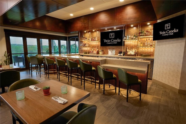 bar featuring a community bar, wood finished floors, and baseboards