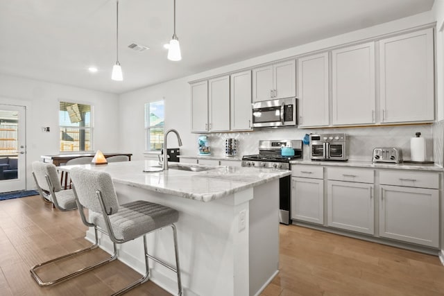 kitchen featuring appliances with stainless steel finishes, light wood-type flooring, a center island with sink, and sink