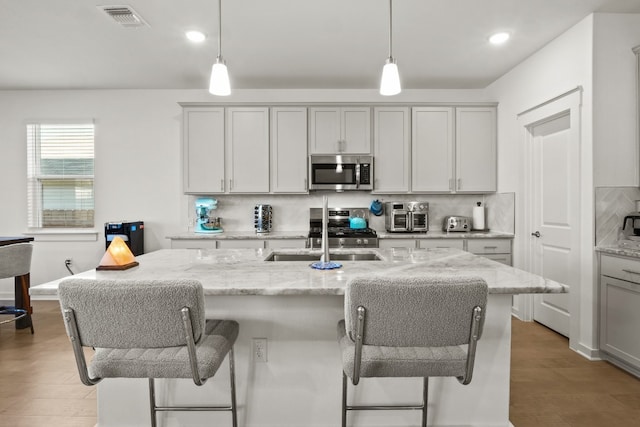 kitchen featuring pendant lighting, light hardwood / wood-style floors, light stone counters, and stainless steel appliances