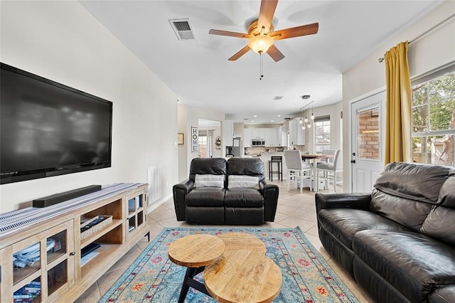 tiled living room with ceiling fan with notable chandelier