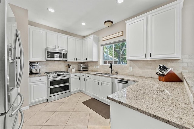 kitchen with sink, light stone counters, backsplash, white cabinets, and appliances with stainless steel finishes