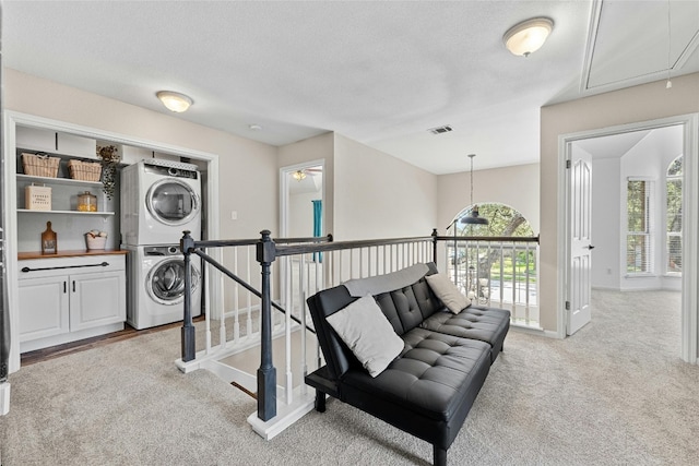 living area featuring a textured ceiling, light carpet, plenty of natural light, and stacked washer / drying machine