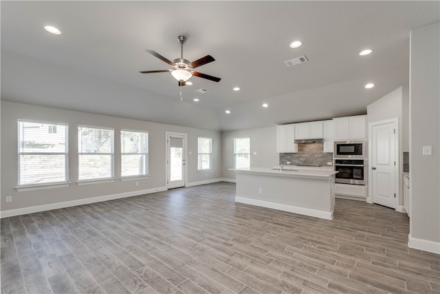 kitchen featuring appliances with stainless steel finishes, vaulted ceiling, a center island with sink, light hardwood / wood-style flooring, and white cabinetry