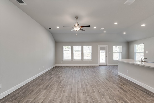 unfurnished living room with ceiling fan, a healthy amount of sunlight, wood-type flooring, and vaulted ceiling