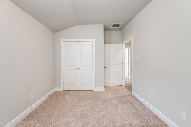 unfurnished bedroom featuring light colored carpet, a closet, and lofted ceiling