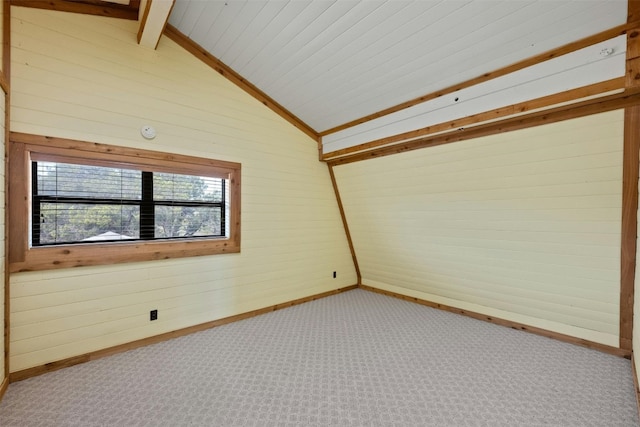 carpeted spare room featuring wooden walls and lofted ceiling with beams