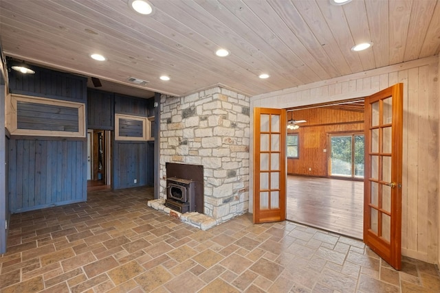 unfurnished living room featuring french doors, wood ceiling, wooden walls, hardwood / wood-style floors, and a wood stove