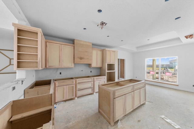 kitchen featuring a raised ceiling, light brown cabinetry, and a textured ceiling