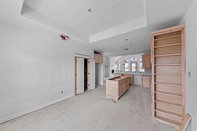 kitchen with light brown cabinetry, a tray ceiling, a kitchen island, and ceiling fan