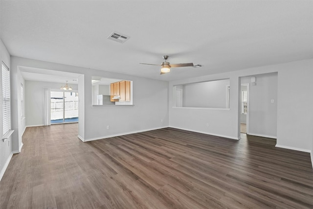 unfurnished living room with ceiling fan with notable chandelier, dark wood finished floors, visible vents, and baseboards