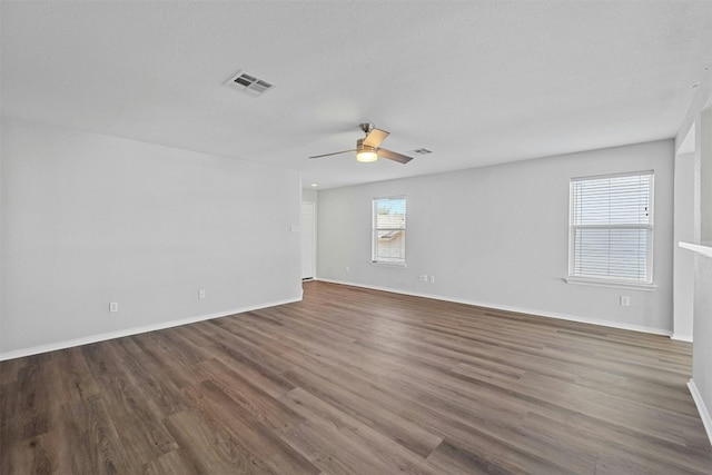 empty room featuring dark wood-style floors, a ceiling fan, visible vents, and baseboards