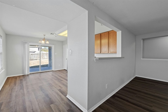 spare room with a notable chandelier, visible vents, baseboards, and wood finished floors