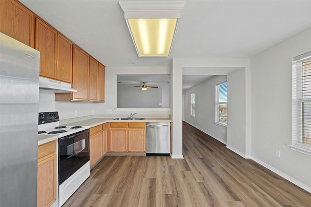 kitchen featuring under cabinet range hood, stainless steel appliances, a sink, wood finished floors, and light countertops