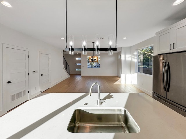 kitchen with white cabinets, decorative light fixtures, stainless steel refrigerator, and sink