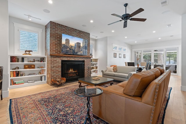 living room with ceiling fan, a fireplace, and light wood-type flooring