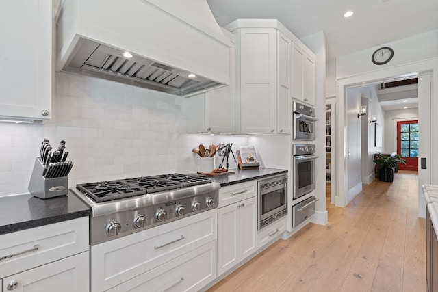 kitchen with stainless steel appliances, premium range hood, tasteful backsplash, and white cabinetry