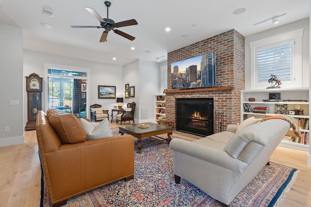 living room with ceiling fan, a brick fireplace, and light hardwood / wood-style floors