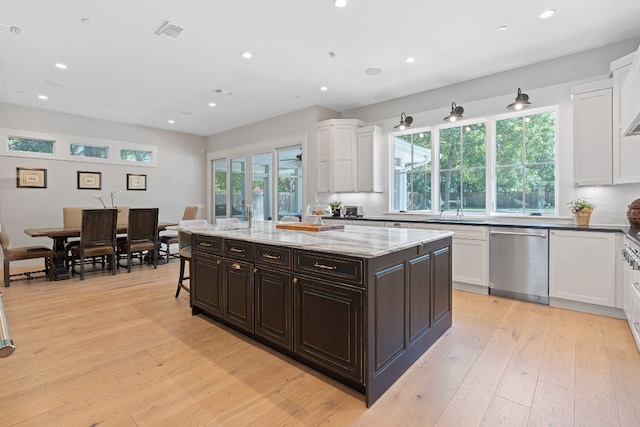 kitchen featuring light hardwood / wood-style flooring, dishwasher, dark brown cabinets, a center island, and light stone countertops