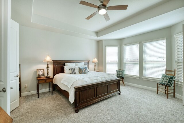 bedroom with ceiling fan, a raised ceiling, and light carpet