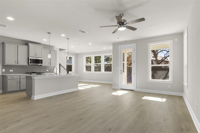 kitchen featuring gray cabinetry, light hardwood / wood-style flooring, backsplash, pendant lighting, and a kitchen island with sink