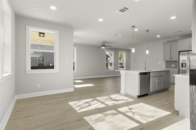 kitchen with gray cabinetry, backsplash, an island with sink, pendant lighting, and appliances with stainless steel finishes