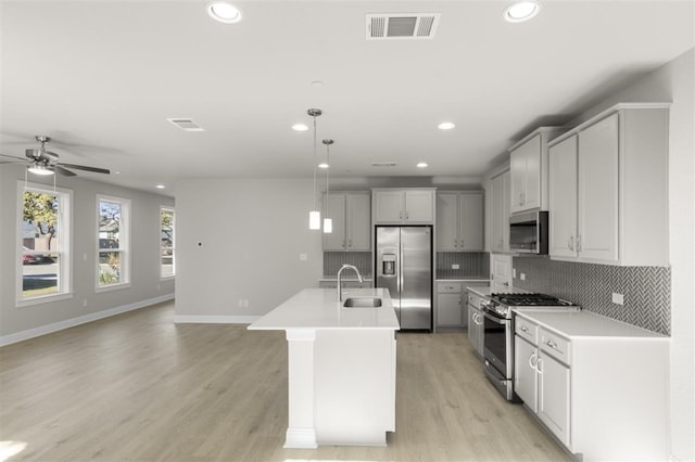 kitchen with a kitchen island with sink, sink, appliances with stainless steel finishes, decorative light fixtures, and light hardwood / wood-style floors