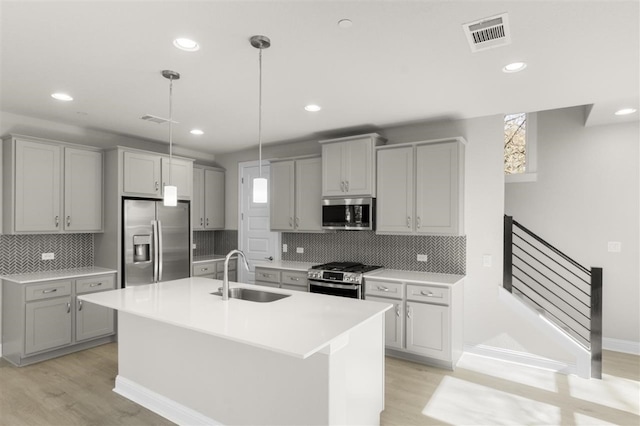 kitchen featuring appliances with stainless steel finishes, gray cabinetry, sink, pendant lighting, and an island with sink