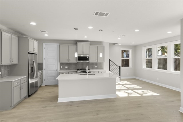 kitchen featuring gray cabinetry, stainless steel appliances, pendant lighting, light hardwood / wood-style floors, and a kitchen island with sink