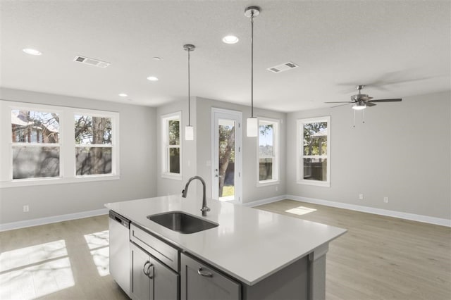 kitchen featuring gray cabinets, sink, decorative light fixtures, and a center island with sink