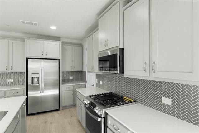 kitchen with white cabinets, backsplash, stainless steel appliances, and light hardwood / wood-style floors