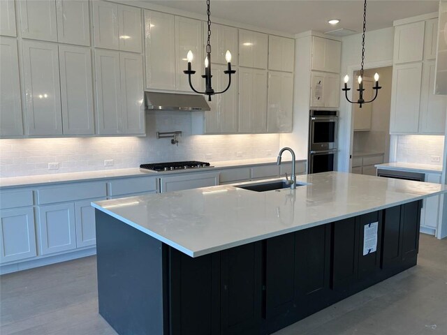 kitchen with stainless steel appliances, white cabinetry, sink, an inviting chandelier, and an island with sink